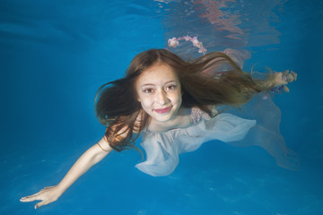 Young beautiful girl in a white dress posing underwater in the pool