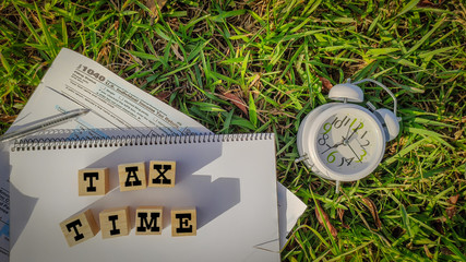 Tax-filling concept - Tax time words on wooden blocks with the U.S IRS 1040 form,pen and clock in...