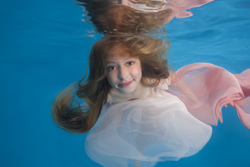 Young beautiful girl in a white dress posing underwater in the pool