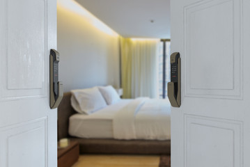 Digital door lock security systems on white wood door in front of blur bedroom background. Electronic door handle with key pads numbers. Selective focus