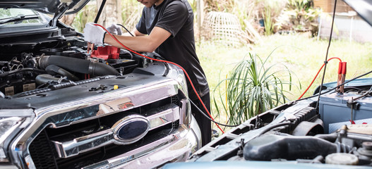 Thai young man is  charging a car battery between two cars using electricity trough jumper cables.