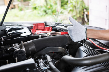 Close up of man hand shows thumb up after charging a car battery using electricity trough jumper cables.