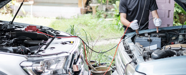 Thai young man is  charging a car battery between two cars using electricity trough jumper cables.