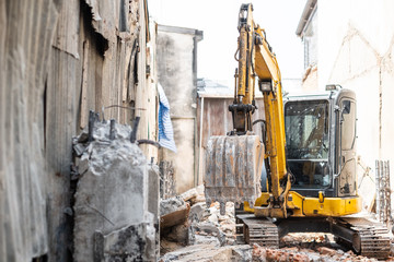 Fototapeta na wymiar Small yellow excavator is on duty for pulling down the old buildings. Selective focus at bucket.