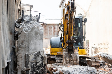 Small yellow excavator is on duty for pulling down the old buildings.