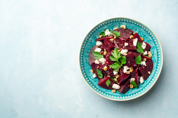 Obraz na płótnie Canvas Healthy beetroot salad with walnuts, feta cheese and parsley on blue concrete background. Top view, copy space.