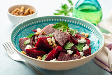 Healthy beetroot salad with walnuts, feta cheese and parsley on blue concrete background. Selective...