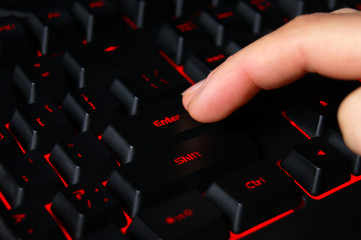 Macro of computer keyboard with finger pressing "enter" key.