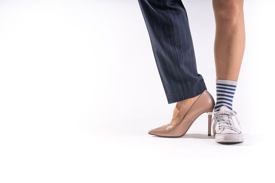 Woman legs with different shoes on each foot on white background. Each leg has a different shoe, one is a white shoe and on the other foot a brown heel shoe
