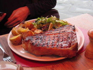 A plate of traditional Florentine steak, potatoes, and salad greens at a restaurant in Florence, Italy 