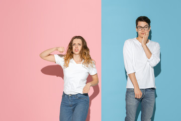 She's dancing, he's calm. Young and happy man and woman in casual clothes on pink, blue bicolored background. Concept of human emotions, facial expession, relations, ad. Beautiful caucasian couple.