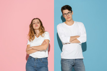 Standing with hands crossed. Young and happy man and woman in casual clothes on pink, blue bicolored background. Concept of human emotions, facial expession, relations, ad. Beautiful caucasian couple.