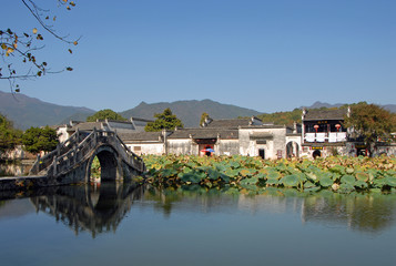 Hongcun Ancient Town in Anhui Province, China. View of the stone bridge crossing Nanhu Lake in Hongcun. Ancient town of Hongcun in China with bridge, old buildings and lilies.