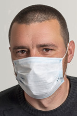 Portrait of a worried middle-aged white young man in a medical mask on gray background