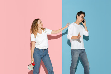 He's talking on phone, she's trying to pay attention. Young and happy man and woman on pink, blue background. Concept of human emotions, facial expession, relations, ad. Beautiful caucasian couple.