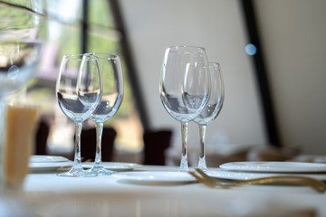 Chic and elegant, gold-plated cutlery and white plates, table setting with empty plates. Glasses in the light from the window. Side view.