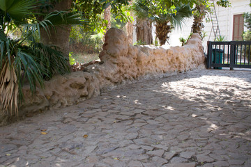 A view of a road that leads to a closed gate, the ground floor of stone, and some trees on one side