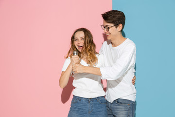 Singing song together. Young and happy man and woman in casual clothes on pink, blue bicolored background. Concept of human emotions, facial expession, relations, ad. Beautiful caucasian couple.