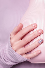 Beautiful female hand holding pink vase on the pale violet background. Manicure with pink color nail polish with shiny design, nude manicure. Copy space