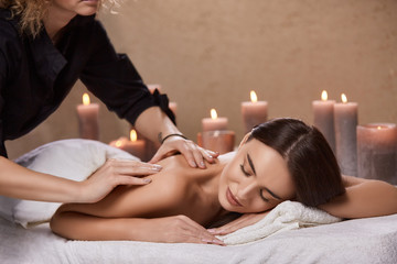 masseur doing massage for woman's back in spa salon with many candles