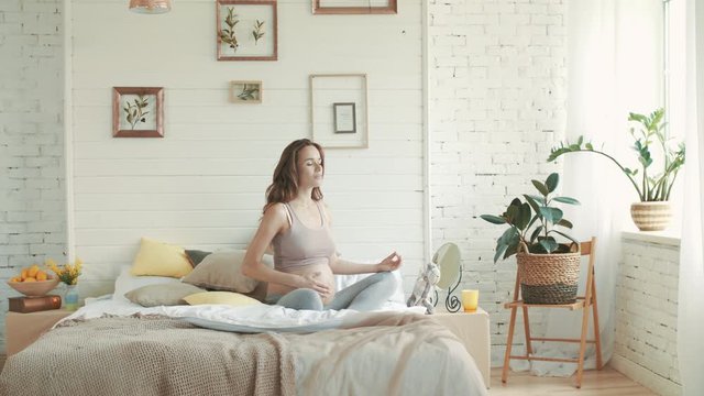 Healthy pregnant woman practicing yoga in bed. Pregant meditating indoors.