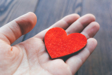 Red colored decorative heart in woman's hand at wooden background. Love concept. Vintage style photo.