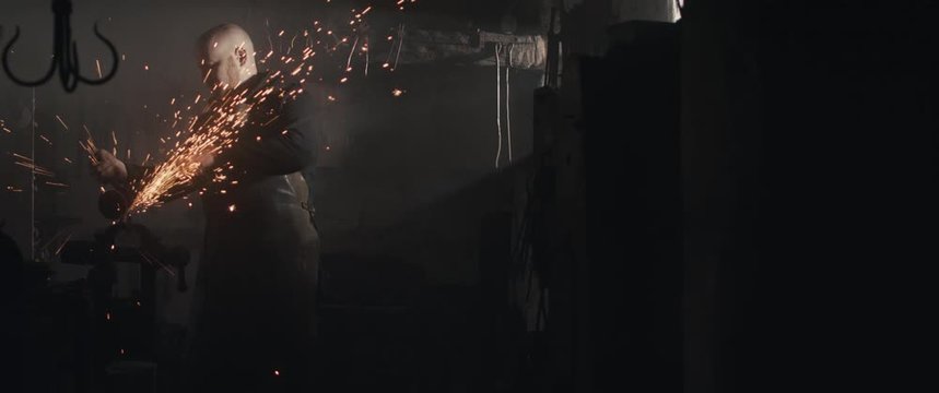 Blacksmith cutting with angle grinder vise sparks dark haze widescreen cinemascope