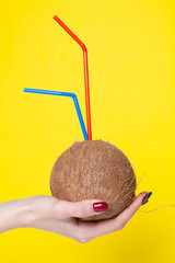 Coconut cocktail in female hands on a yellow background.