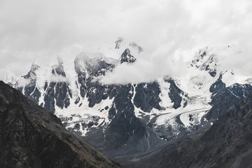 Obraz premium Atmospheric alpine landscape with massive hanging glacier on giant mountain. Big glacier tongue on mountainside. Low clouds among snowbound mountains. Cracks on ice. Majestic scenery on high altitude.