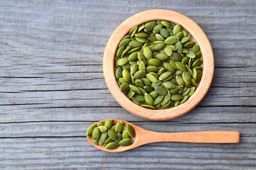 Raw peeled pumpkin seeds in a wooden plate and spoon on the table.Healthy eating,diet or vegan food concept.Top view.Copy space.Selective focus.