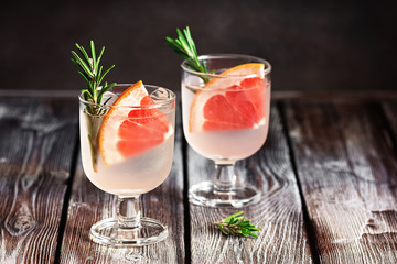 Refreshing drink with grapefruit and rosemary in a glass on a wooden rustic table. Selective focus. Summer cold beverage.