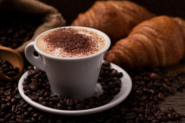 Cappuccino and croissant with coffee beans close up