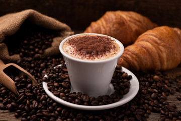 Cappuccino and croissant with coffee beans close up