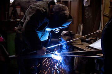 welder in mask, in the process of welding metal with bright light, smoke and sparks