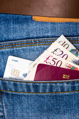 Closeup of fifty, twenty, ten pounds sterling banknotes, contactless credit card and EU passport peeking out of blue jeans back pocket