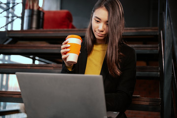 Young asian female entrepreneur deep in thought while working at laptop computer in a modern loft...