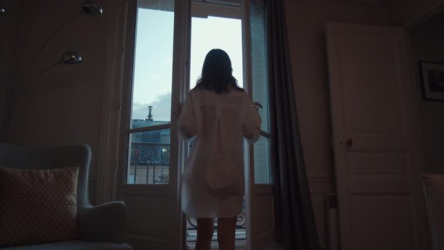 Attractive woman opening the door to the balcony with a view of Paris