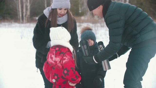Happy family drinking tea from the termos outdoors near the forest