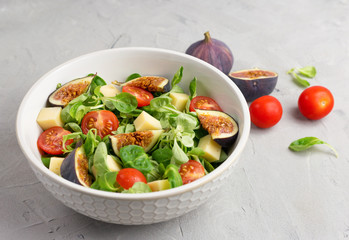 Fresh salad with figs, green leaves, cherry tomatoes and cheese on gray background. Free space for text. Top view. Abstract food background with big plate