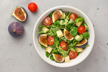 Fototapeta na wymiar Fresh salad with figs, green leaves, cherry tomatoes and cheese on gray background. Free space for text. Top view. Abstract food background with big plate