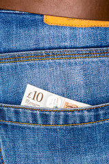 Closeup of ten pounds sterling banknote peeking out of blue jeans back pocket