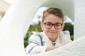 Close up portrait of a brunette boy whit glasses wearing a fashion white sailor suit for his first...