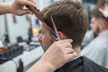 Master hairdresser cuts hair on the head of a young bearded guy. Close-up of the hand of a professional haircutter with scissors in a barber shop.
