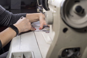 close-up of the hands of a seamstress sewing clothes, sews fabric behind a sewing machine