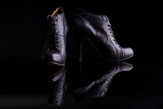 Black women's ankle boots on a black surface reflecting the ankle boots. The photo is taken in a photo studio with flash light illuminating the boots and on a black background