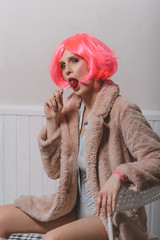Young attractive woman in a bright pink wig, golf and faux fur coat.