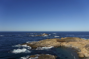 Looking out over the rocky coast of Big Sur and the blue Pacific Ocean under a clear blue sky; horizon