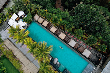 Aerial view of luxury pool with umbrellas and swimming around palm trees and jungle.Vacation concept. Drone photo