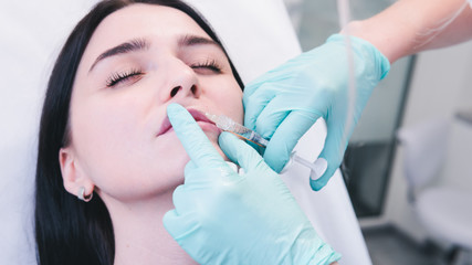 Beautician hands making botox injection in female lips. The doctor cosmetologist makes lip...