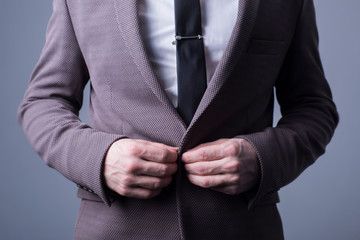 studio portrait of a young bearded handsome guy of twenty-five years old, in an official suit, buttoning a button in a jacket. On a dark background. Office Style. Fashion and office